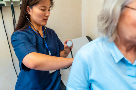 Female doctor using stethoscope examining lungs of senior patient during medical checkup in hospital...