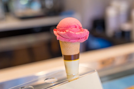 Refreshing pink ice cream scoop melting on crispy cone, displayed on showcase in ice cream shop,...