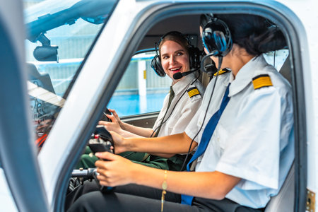 Two smiling female pilots wearing headsets and uniforms are sitting in the cockpit of a small aircraft, operating controls and communicatingの写真素材