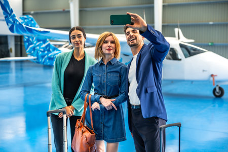 Three businesspeople are taking a selfie with a smartphone in a hangar with a private jet and luggageの写真素材