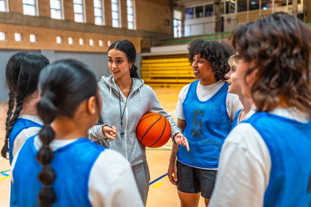 Female basketball coach holding ball and explaining game strategy to her team during training in a gymnasiumの写真素材