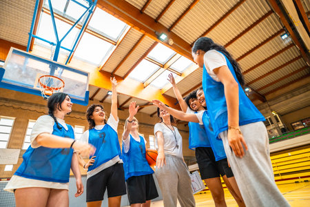 Basketball players and their coach celebrating a victorious moment with high fives in a vibrant gymnasium filled with energy and excitementの写真素材
