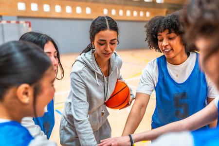 Female basketball coach motivating and inspiring her team during a time out, holding the ball and putting their hands togetherの写真素材