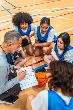Basketball coach explaining game strategy to female athletes on a clipboard, during a time out in a basketball courtの写真素材
