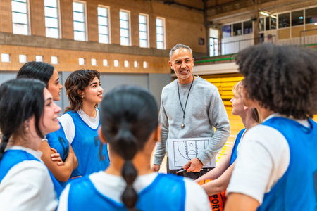 Basketball coach holding clipboard and explaining game strategy to a group of female athletes in a gymnasiumの写真素材
