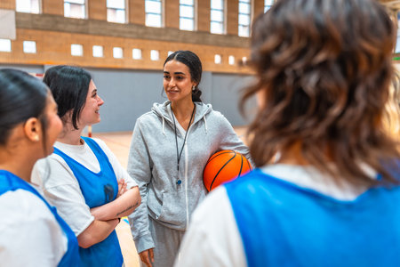 Female basketball coach holding a ball and engaging with her team during an intense training session in the gym, fostering teamwork and motivationの写真素材