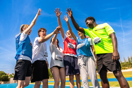 Group of young athletes celebrating their victory on a running track, raising hands together in a display of teamwork and sportsmanshipの写真素材