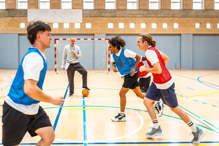 Group of young basketball players running on the court during practice, with their coach watching...