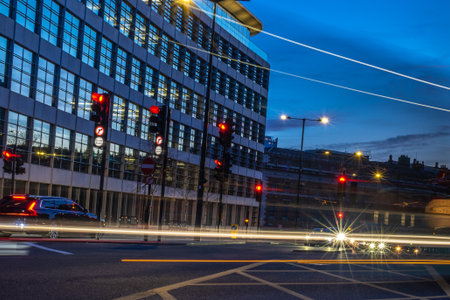 Cars passing by on a London street at dusk, with traffic lights turning red and offices in the backgroundの写真素材