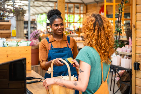 Friendly shop assistant holding credit card reader while customer making contactless payment in a...