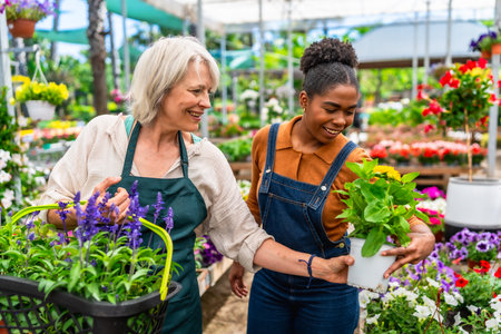 Two happy multiethnic female garden center workers carrying plants and flowers in a greenhouseの写真素材