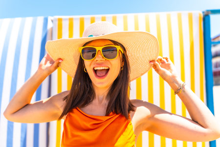 Young woman wearing a straw hat and sunglasses, smiling brightly while enjoying the summer sun,...