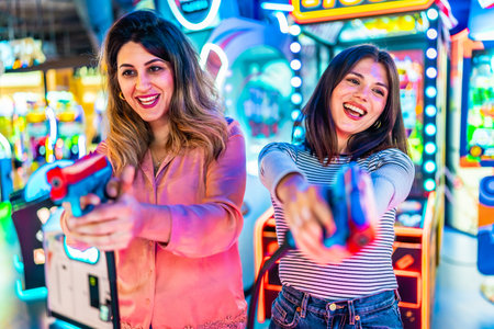 Two young women enjoying their free time playing together in an amusement arcade, holding toy guns and having funの写真素材
