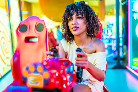 Young woman enjoying a car racing arcade game, holding the steering wheel and focused on the screen in a colorful, illuminated entertainment centerの写真素材