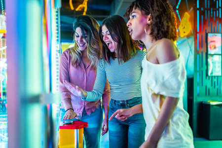 Three young women enjoying their time together at an amusement arcade, playing games and having fun in a vibrant, colorful atmosphereの写真素材