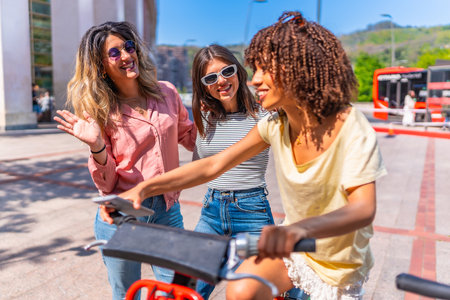 Three cheerful young women using smartphone and riding a sharing bike in a city center during summer holidaysの写真素材