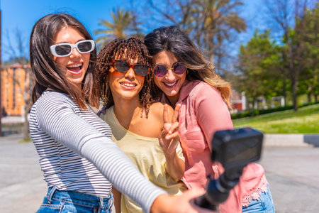 Three cheerful young women making peace sign and taking selfie with action camera during summer vacation in the cityの写真素材