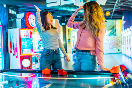 Two women giving high five while playing air hockey, enjoying their time together in entertainment venueの写真素材