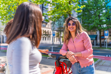 Group of friends talking and smiling next to a red electric scooter in a sunny summer day in the cityの写真素材