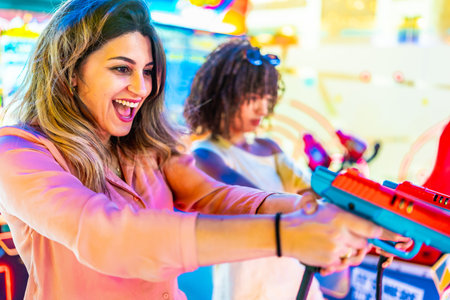 Two young women enjoying their summer vacation, playing arcade shooting games and having fun togetherの写真素材