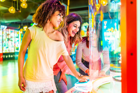 Three cheerful female friends enjoying their time together playing an arcade game in an amusement parkの写真素材