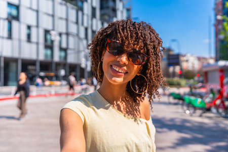 Smiling tourist enjoying a sunny day in the city, capturing the moment with a selfie while soaking up the vibrant urban atmosphereの写真素材