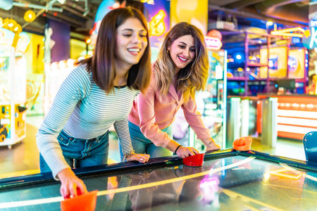 Two young women enjoying their free time playing air hockey in a colorful and modern amusement arcadeの写真素材