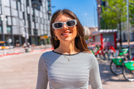 Portrait of a happy young woman wearing sunglasses and a striped shirt in a city center during a sunny summer dayの写真素材