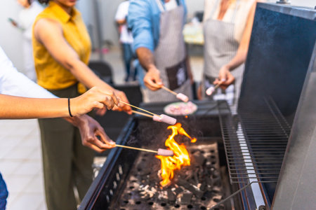 Friends are grilling marshmallows on skewers over a barbecue fire, enjoying a summer cookout togetherの写真素材