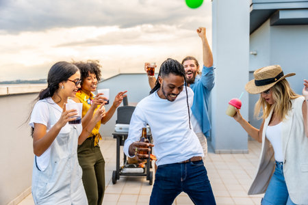 Young people enjoying a vibrant rooftop party, dancing, laughing, and sipping drinks while savoring delicious barbecue under the sunset skyの写真素材
