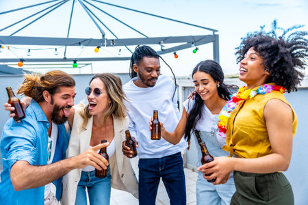 Cheerful multi ethnic friends laughing and enjoying drinks while celebrating together at a lively rooftop party under the summer skyの写真素材