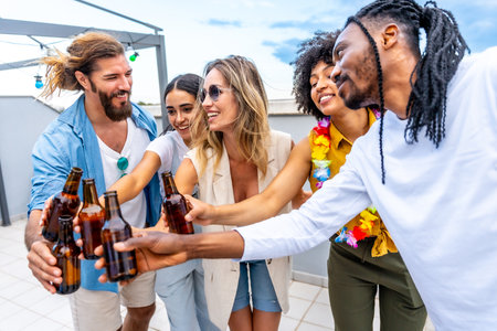 Happy friends celebrating on a rooftop, toasting with beer bottles and enjoying quality time together in a vibrant summer atmosphereの写真素材