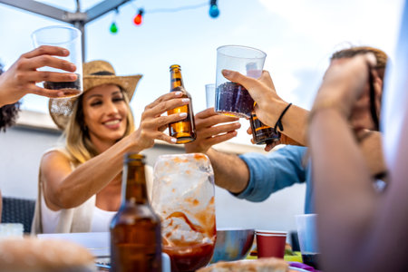 Cheerful friends raising glasses and bottles, making a toast during a rooftop party, celebrating their friendship with joy and excitementの写真素材
