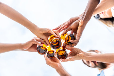 Group of friends toasting with beer bottles against a bright sky, celebrating friendship and enjoying a refreshing moment togetherの写真素材