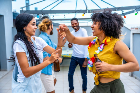 Cheerful young friends are dancing and having fun at a rooftop party, enjoying drinks and each other's companyの写真素材