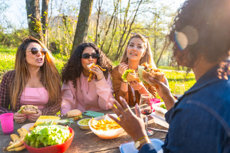 Group of friends having fun eating and drinking outdoors on a sunny day, celebrating friendship and good times togetherの写真素材