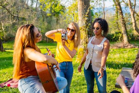 Group of friends soaking up the sun in nature, playing music, capturing moments with cameras, and enjoying each other's companyの写真素材