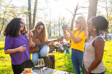 Multi ethnic women having fun at picnic, playing guitar, taking pictures and singing togetherの写真素材