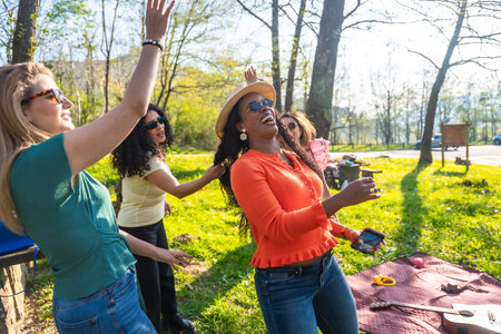 Four women dancing and enjoying themselves during a picnic in a park, celebrating friendship and leisure timeの写真素材
