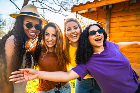 Four multi ethnic female friends are enjoying a sunny day in a garden, smiling and embracing each otherの写真素材