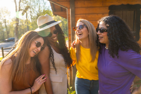 Four diverse women wearing sunglasses and casual clothes are enjoying a sunny day in nature, laughing and embracing each otherの写真素材