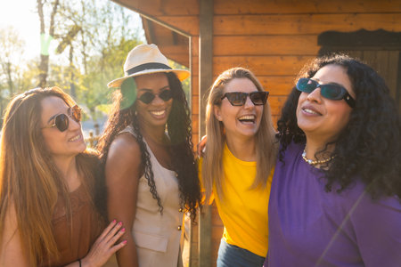 Four multi ethnic female friends are enjoying a sunny day together, laughing and embracing outdoorsの写真素材