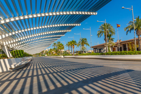 Sunlight filtering through a contemporary pergola creating striking shadows on a Spanish promenade, adding an artistic touch to the urban landscapeの写真素材