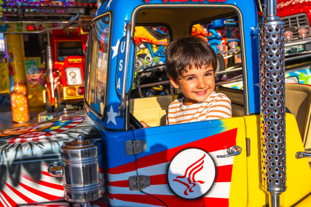 Young boy with a joyful expression sitting in a colorful amusement park ride, surrounded by bright and festive decorationsの写真素材