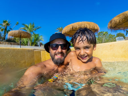 Happy father and son are spending quality time together, playing in swimming pool during summer vacationの写真素材