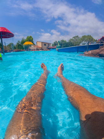 Pov shot of a man relaxing in a swimming pool at a water park, enjoying the summer sun and the refreshing waterの写真素材
