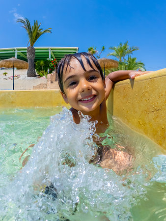 Smiling child splashing joyfully in a swimming pool, relishing carefree summer vacations at a vibrant tropical resortの写真素材