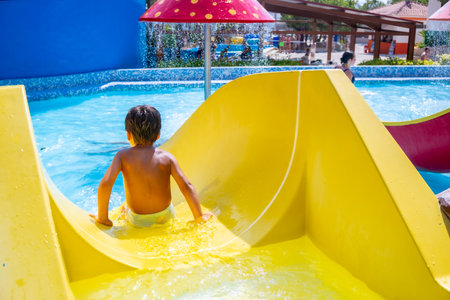 Young boy enjoying a thrilling ride down a vibrant waterslide at a lively water park, embracing the excitement of summer vacationの写真素材
