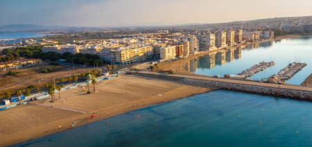 Aerial view of the cityscape of Torrevieja reflecting on the calm water of the Mediterranean sea with naufragos and acequion beach at sunriseの写真素材