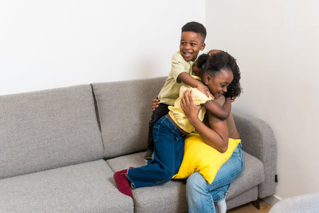 Two joyful children hugging their mother, sitting on a comfortable sofa in their living room, enjoying a loving family momentの写真素材